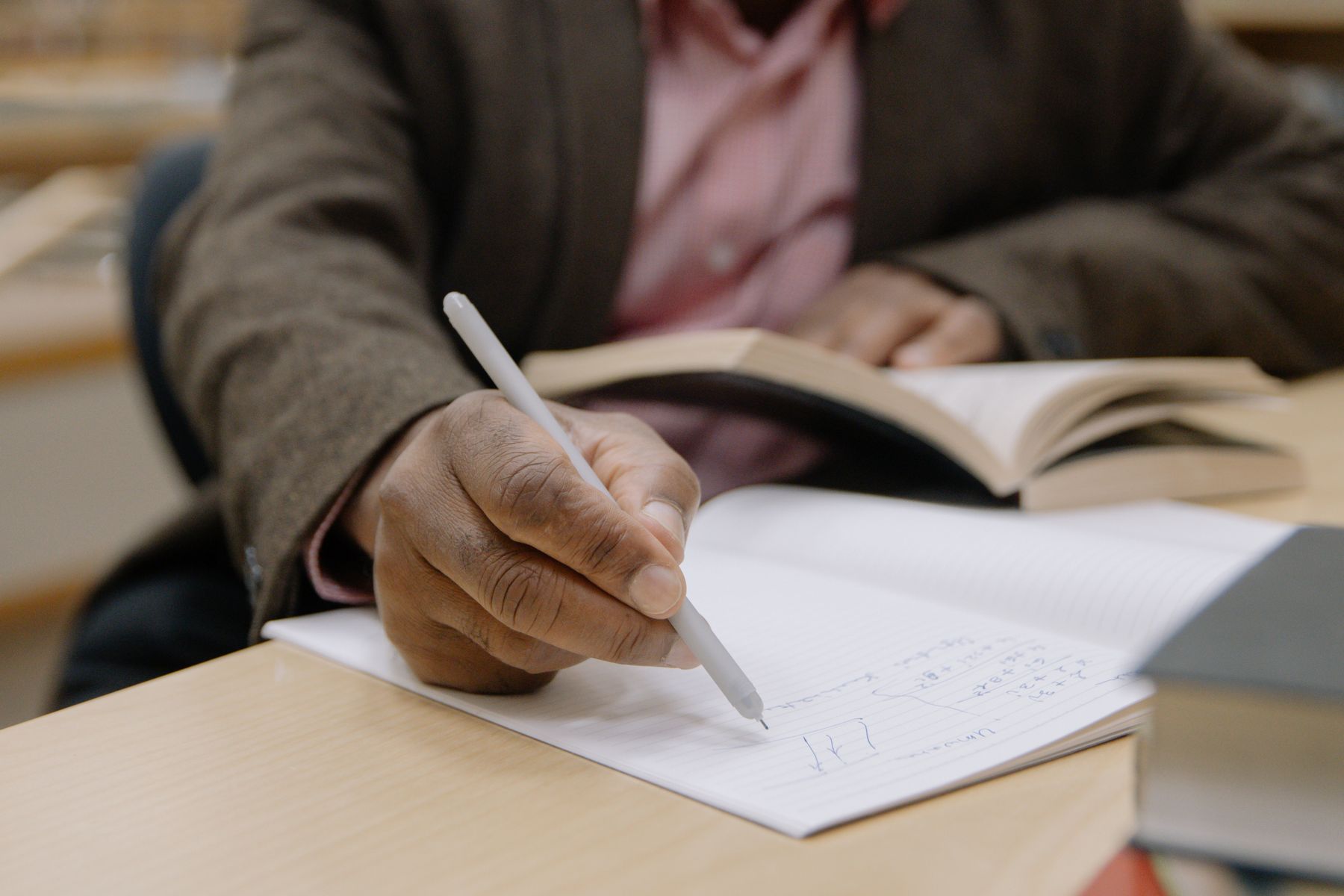 A person writing notes beside an open book in a library.
